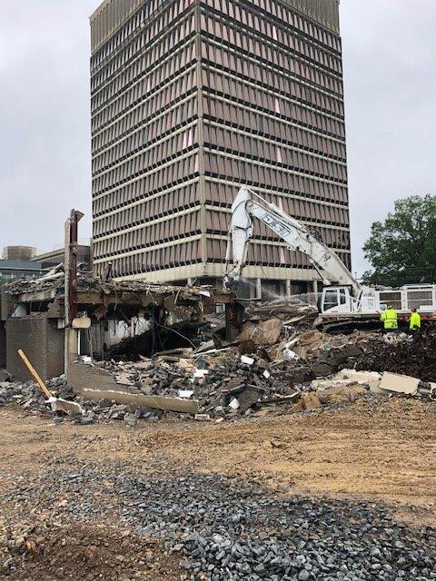 Demolished building with rubble and excavator in front of a tall office tower