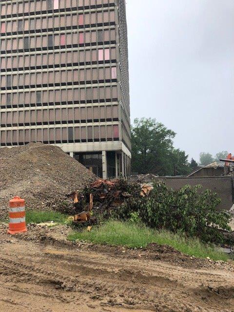 Construction site with dirt road, orange barrel, debris pile, and tall office building in the background