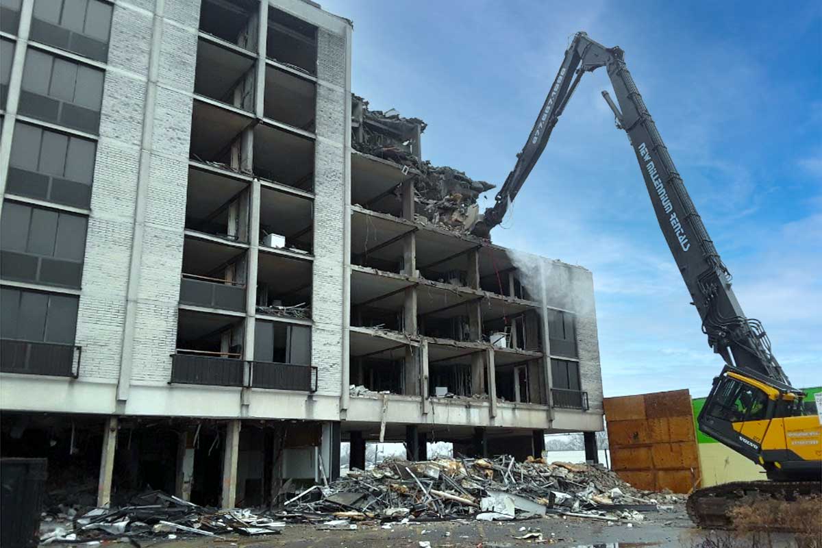 Demolition of a concrete building with an excavator and debris scattered in front