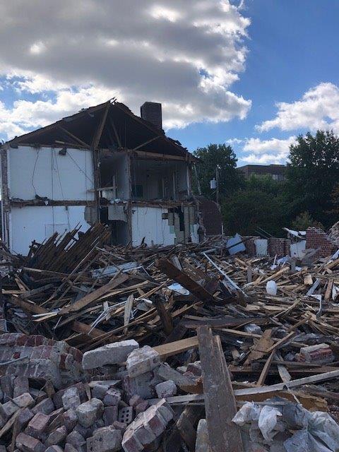 Partially collapsed house with rubble and bricks scattered in the foreground under a cloudy sky