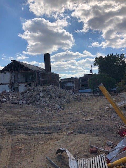Rubble and damaged buildings at a construction or demolition site under a cloudy blue sky.