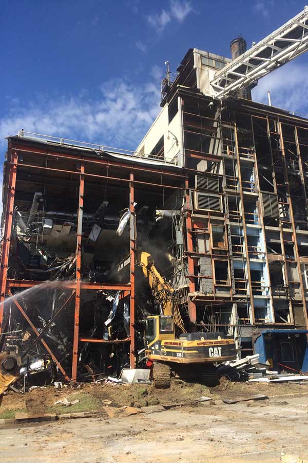 Damaged industrial building with scaffolding and a conveyor structure under a blue sky