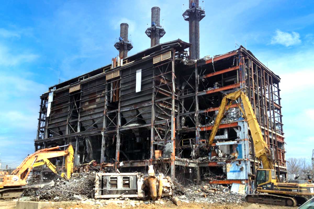 Industrial building under construction with two yellow excavators and exposed steel framework under a blue sky