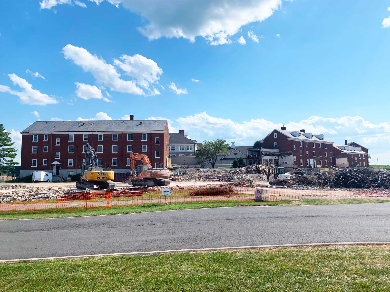 Red brick apartment buildings under a bright blue sky beside a construction site and road