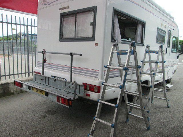Camper bianco con portabici e due scale appoggiate. Ambiente esterno.