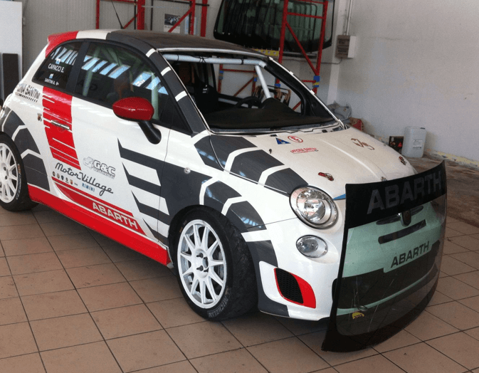 Un'auto da corsa Abarth bianca e rossa con dettagli neri e grigi, parcheggiata al chiuso.