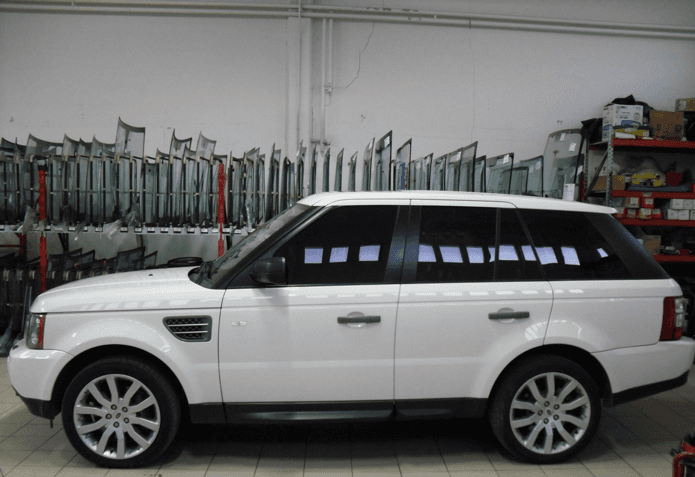 Range Rover Sport bianca in un garage, con vetri oscurati e parabrezza sostitutivi sullo sfondo.