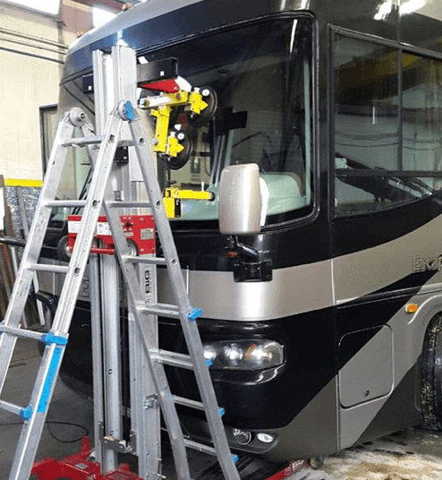 Un camper con un nuovo parabrezza viene installato utilizzando un sollevatore e una scala all'interno di un'officina.