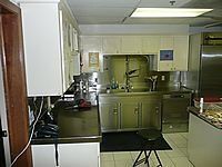 Small kitchen with green cabinets, white appliances, tiled floor, and a counter with dishes.