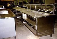 Metal kitchen worktables and shelves in a commercial kitchen, shown in a dimly lit room.
