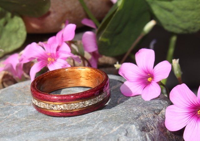 A wooden memorial ring rests on a stone with tiny pink flowers behind.