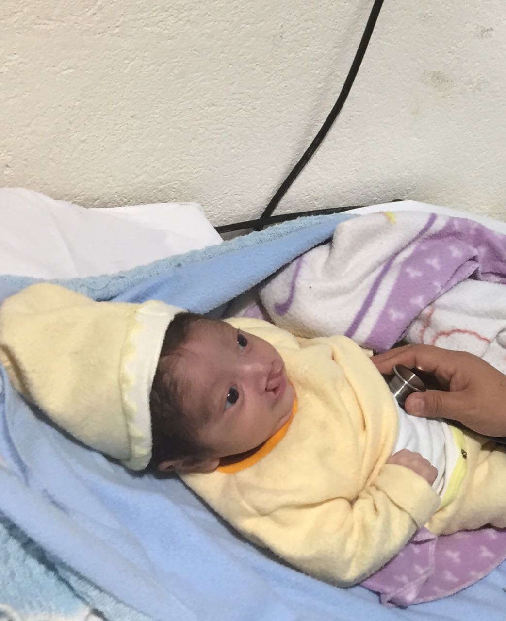 Ein Baby mit einer gelben Mütze liegt auf einer blauen Decke