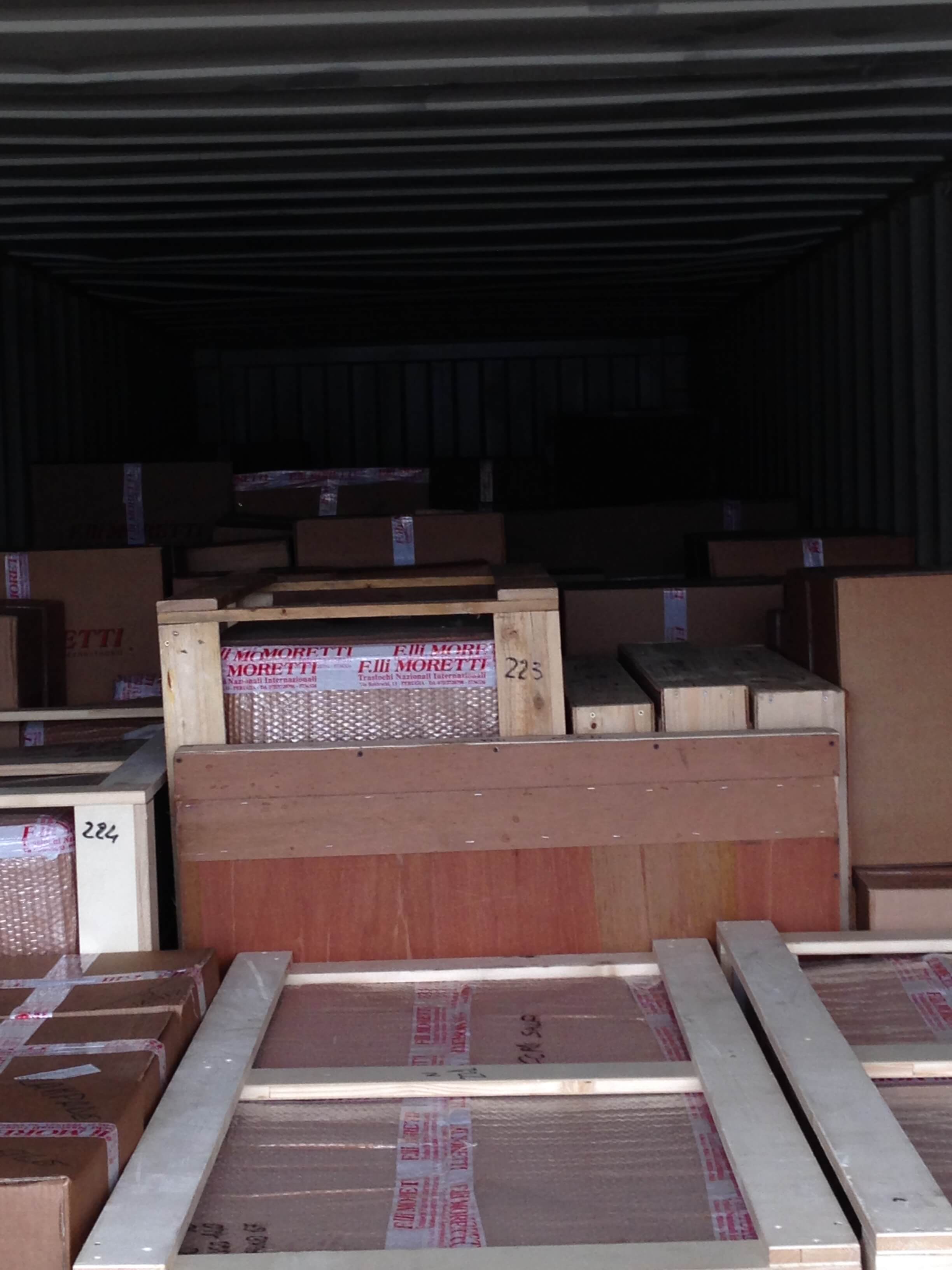 Interno di un container pieno di scatole di cartone e casse di legno impilate.
