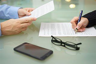 A person is signing a document while another person looks at it.