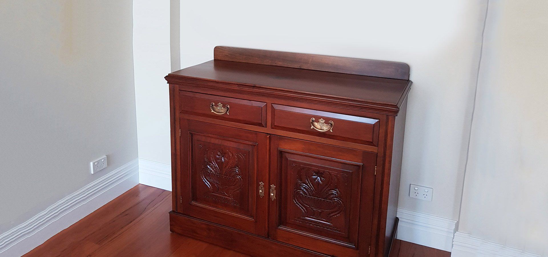 A wooden cabinet with two drawers and carved doors in a room with hardwood floors.