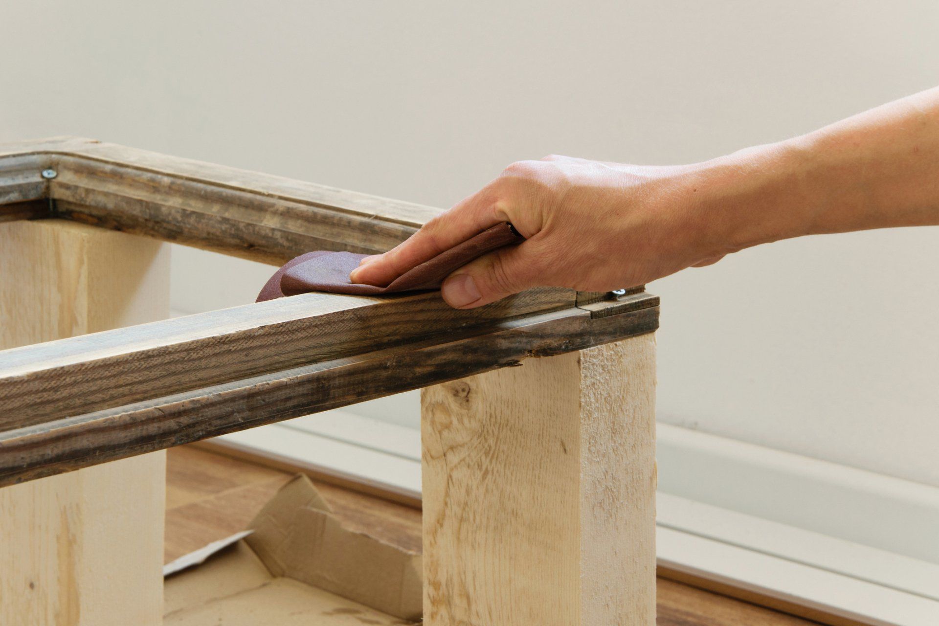 Person sanding a wooden frame with a sanding block indoors, preparing it for refinishing.