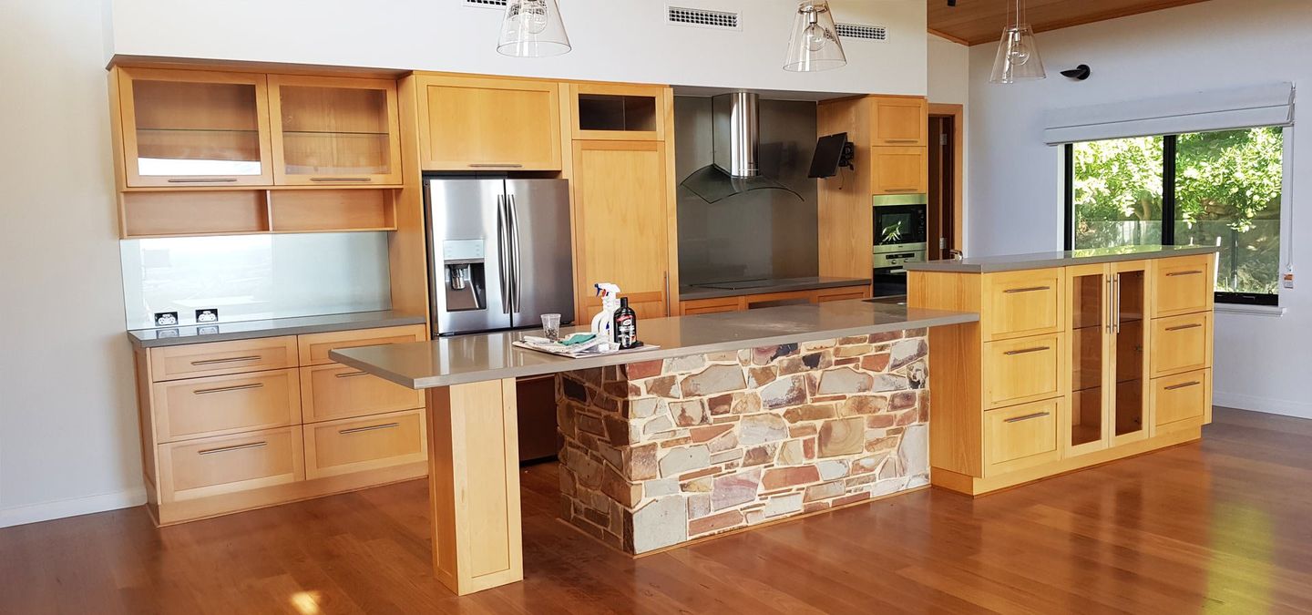 A kitchen with light wood cabinets, stainless steel appliances, and a stone island.