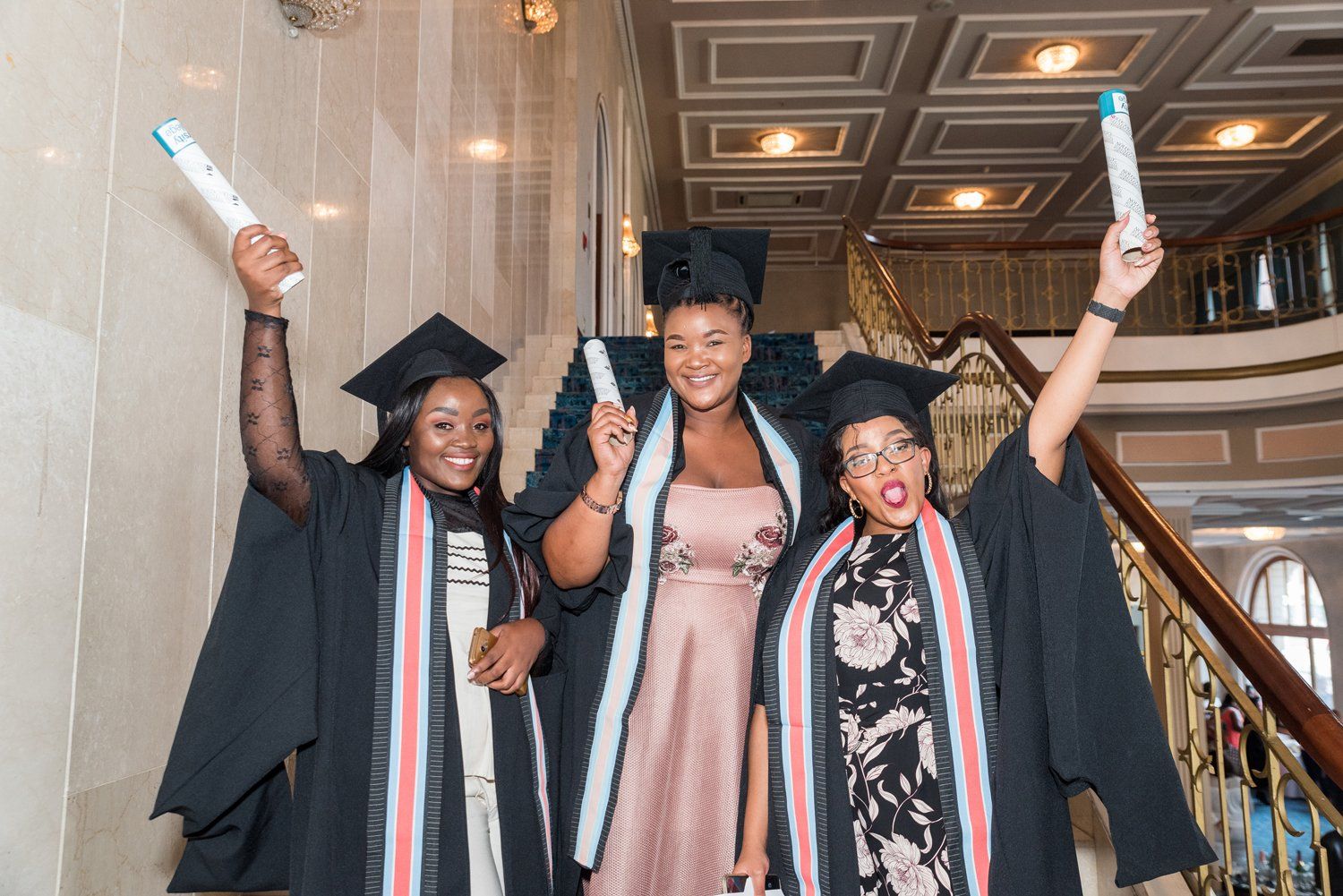 Three female graduates are posing for a picture while holding their diplomas in the air.