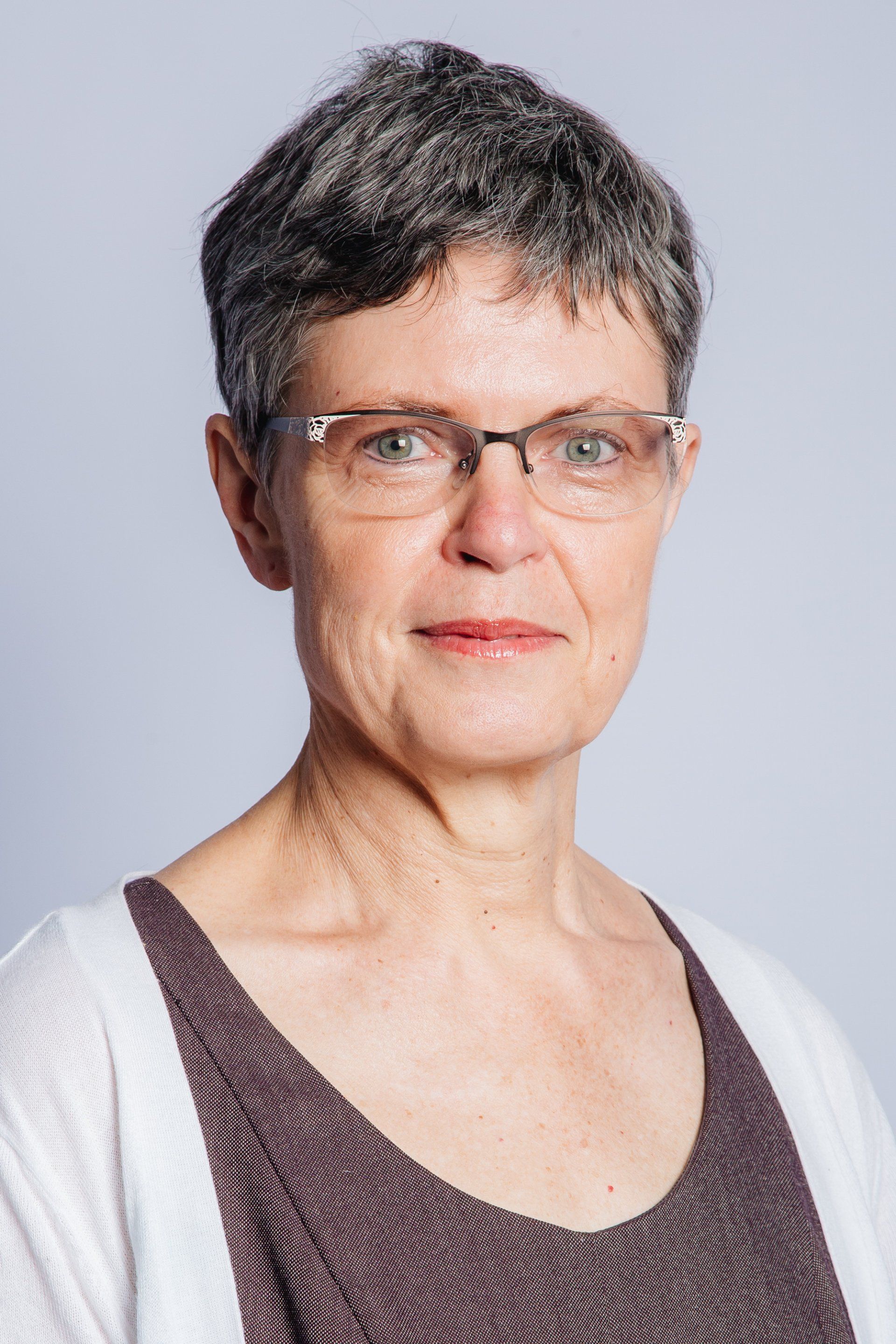 A woman wearing glasses and a white sweater is smiling for the camera.