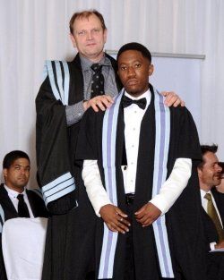 A man in a tuxedo stands next to another man in a gown