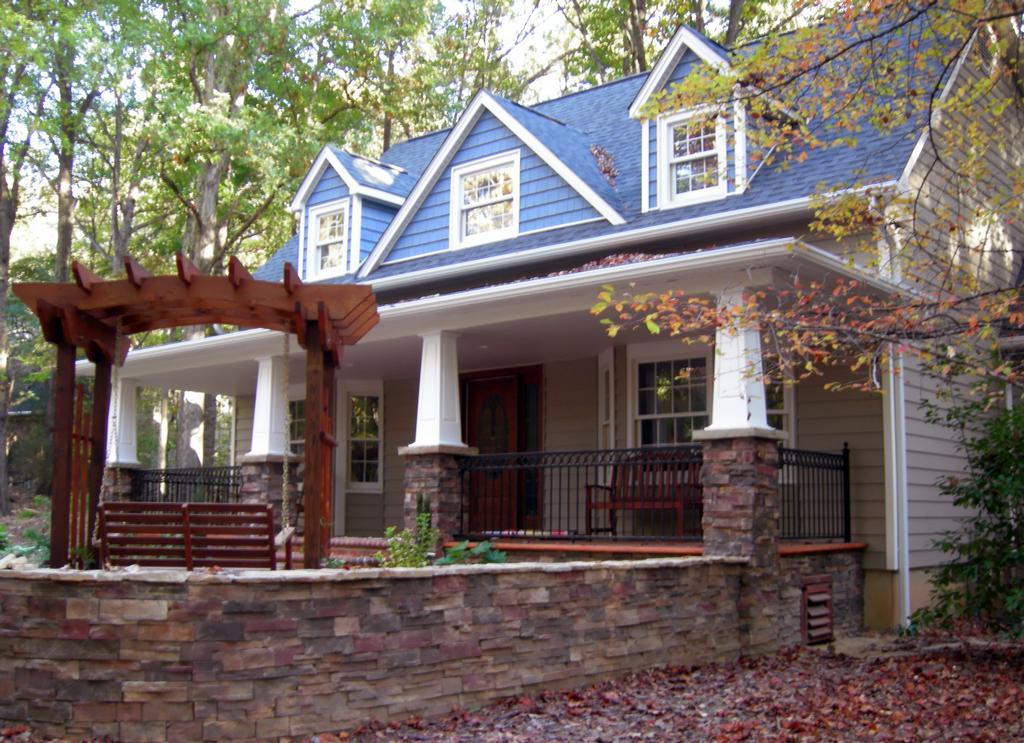 Blue-roofed house with stone porch, white columns, and wooden pergola in a leafy yard