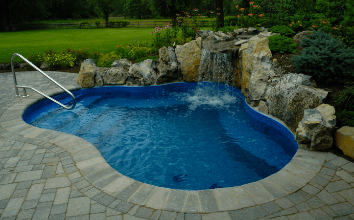 Curved backyard pool with blue water beside rocks and a small waterfall.