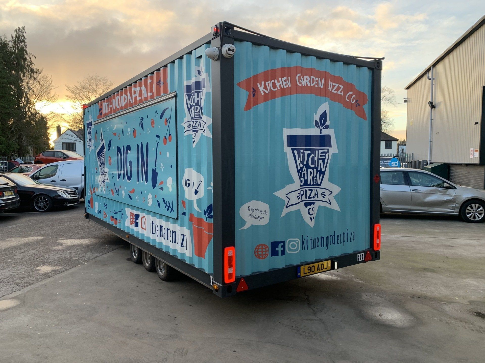 A blue trailer is parked in a parking lot next to a building.