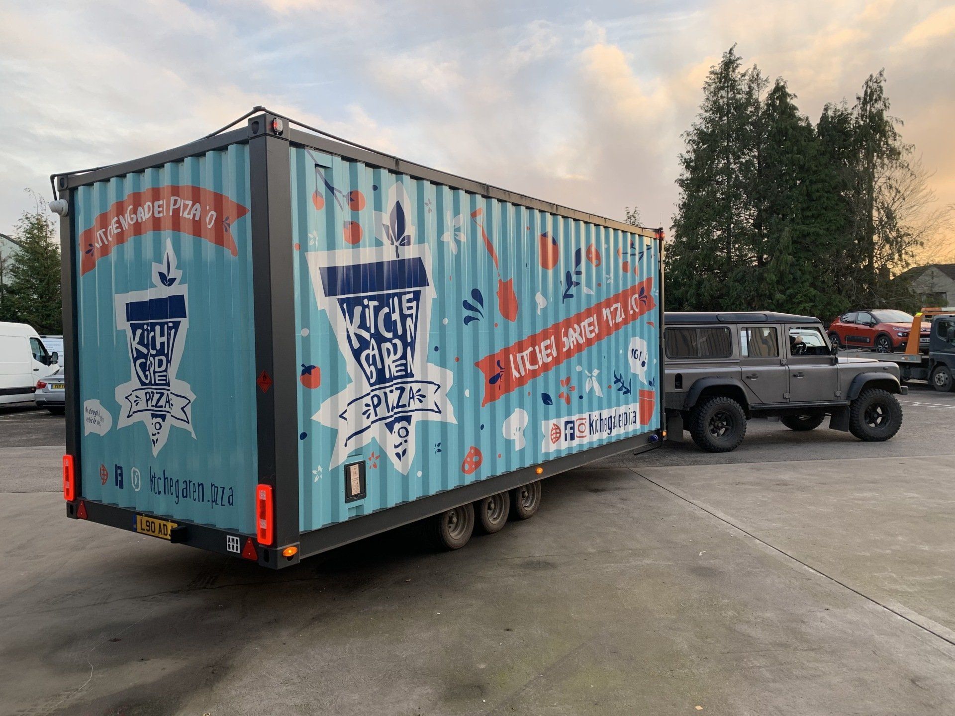 A blue shipping container is being pulled by a truck in a parking lot.