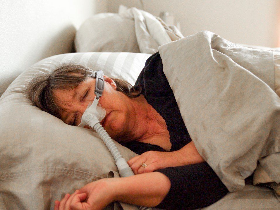 Person sleeping in bed with a nasal oxygen mask under white covers