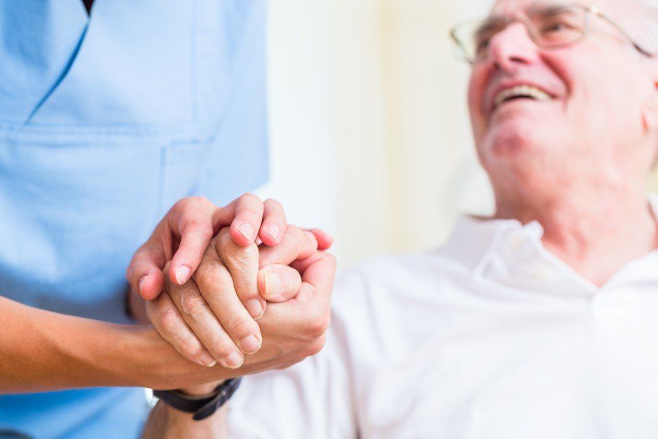 Healthcare worker holding a smiling patient’s hand in a bright hospital room