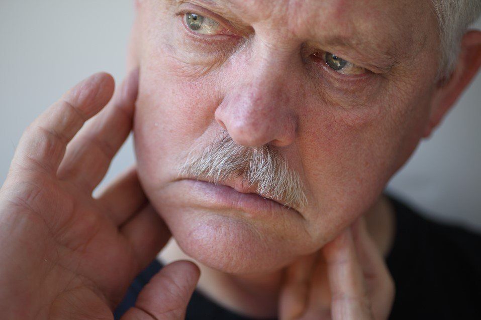 Close-up of a man touching his neck and looking thoughtfully to the side.