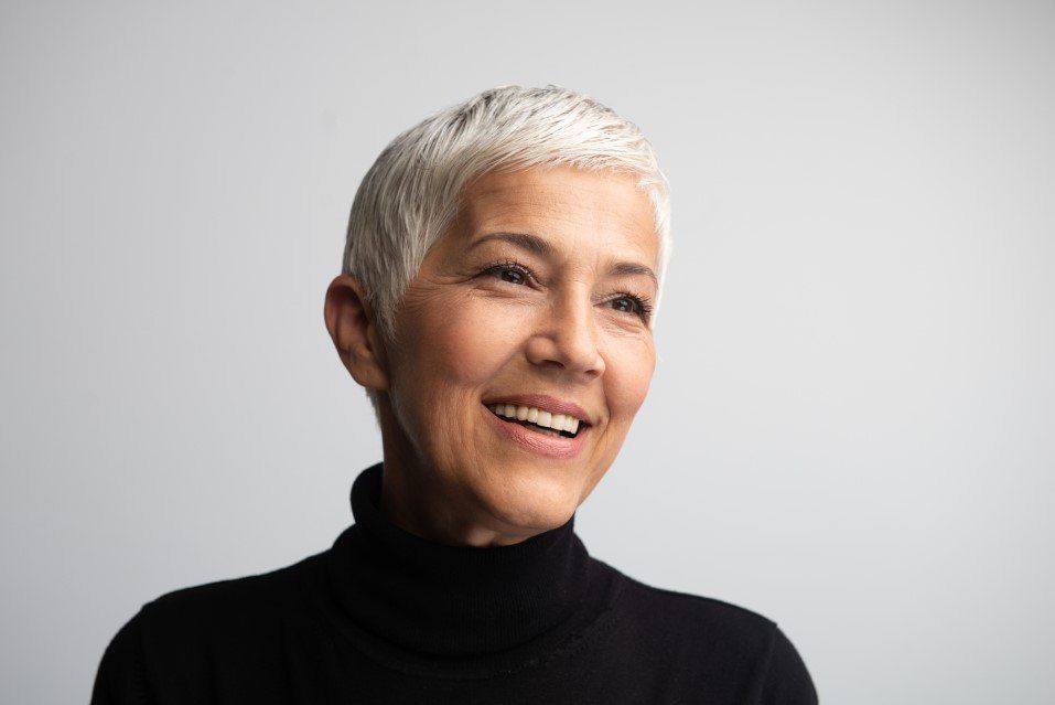 Smiling person with short silver hair wearing a black turtleneck against a light gray background