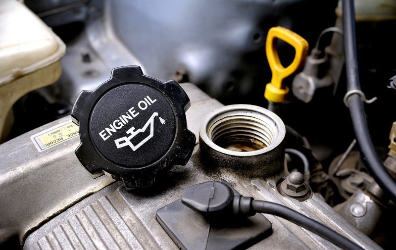 Open engine oil cap and yellow dipstick on a car engine