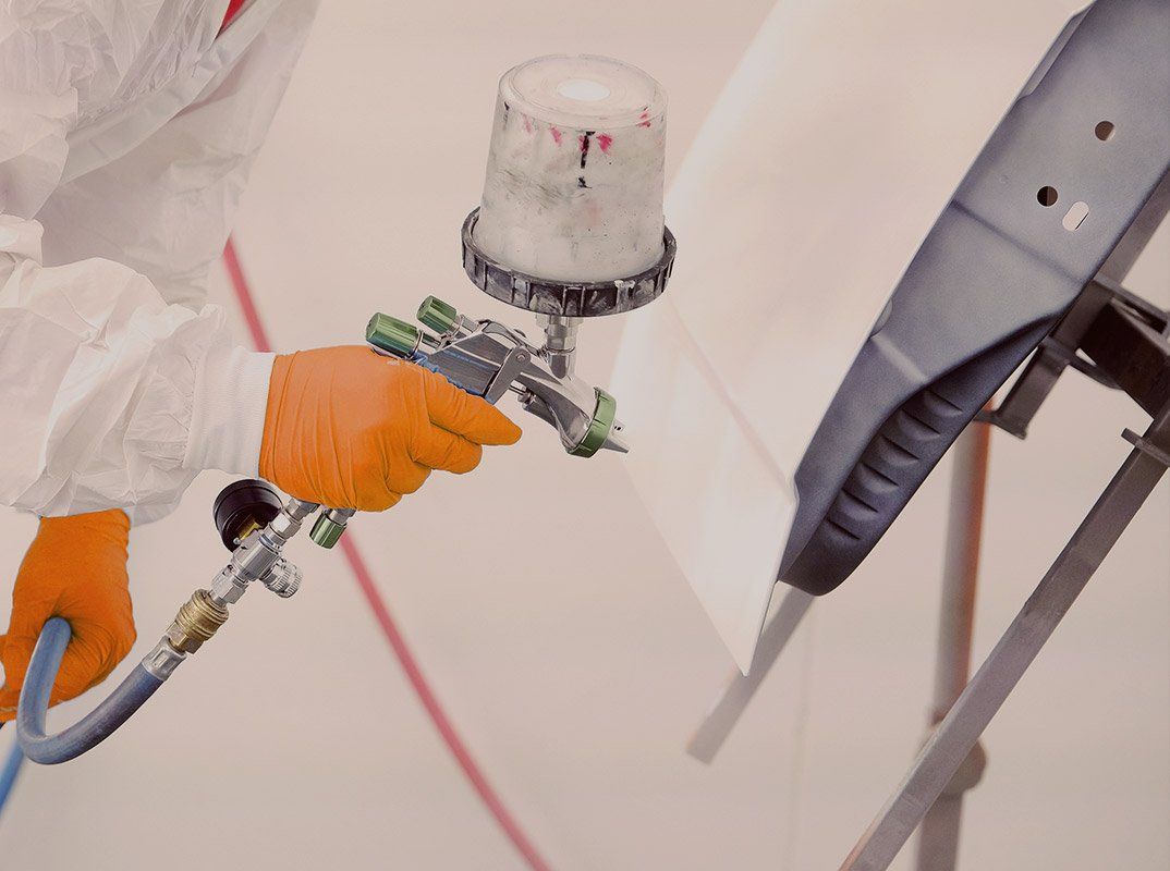 Person in orange gloves spray-painting a white vehicle with a paint gun and air hose