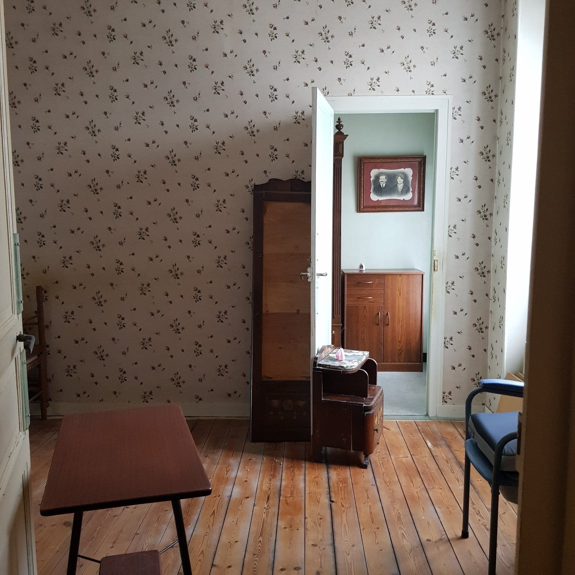 chambre avant rénovation avec un vieux miroir et du papier peint délavé