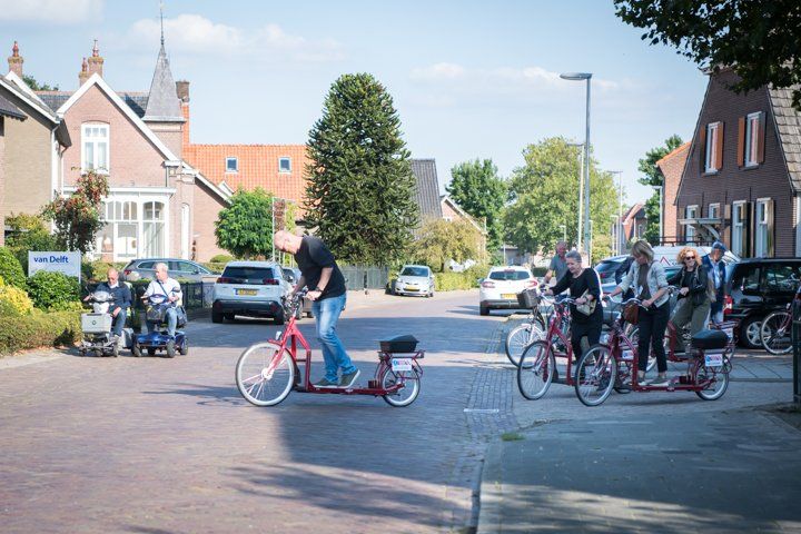 Mensen op bijzondere fietsen en scootmobielen in een woonwijk.