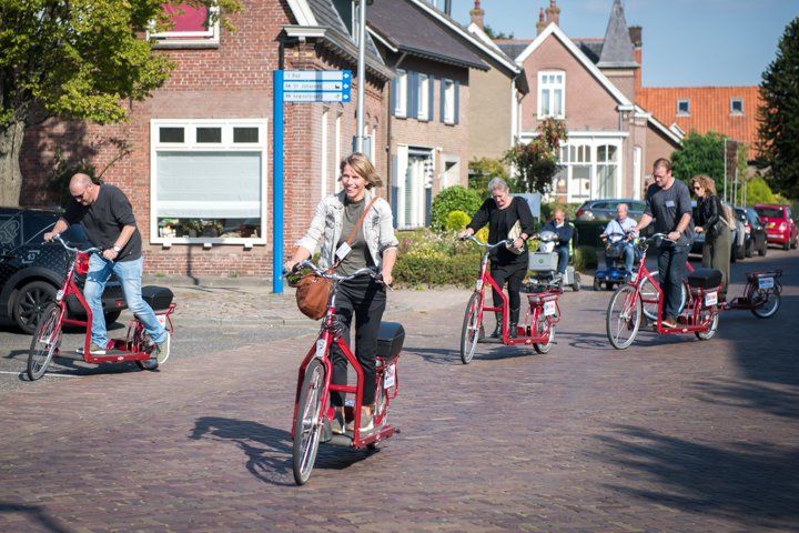 Mensen rijden op rode scooters door een straat voor bakstenen gebouwen op een zonnige dag.
