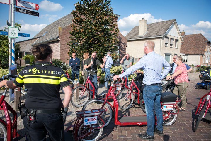 Een politieagent en een groep mensen staan ​​naast rode fietsen in een stedelijke omgeving. Een man gebaart naar de fietsen.