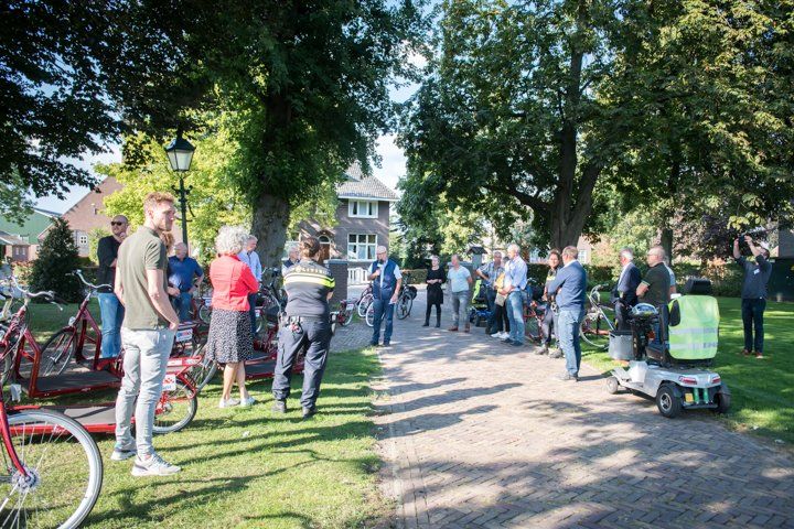 Een groep mensen had zich buiten verzameld, sommigen bij fietsen, met een politieagent in het midden.