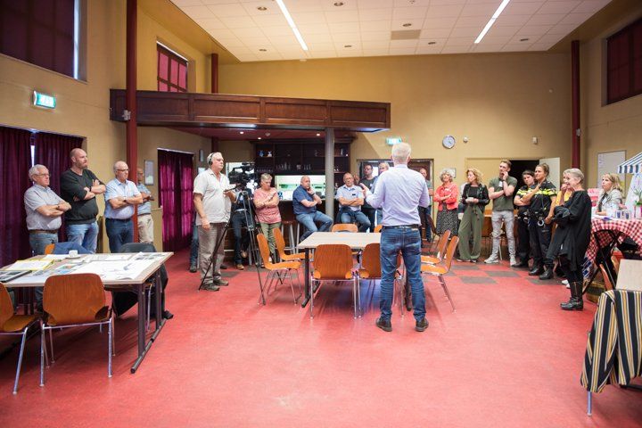 Een man spreekt een groep mensen toe in een grote zaal. Mensen staan ​​en zitten en luisteren.