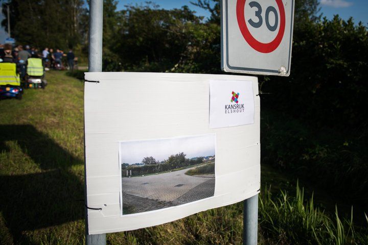 Bord met snelheidslimiet van 30 km/u, afbeelding van de weg en logo op een metalen paal.