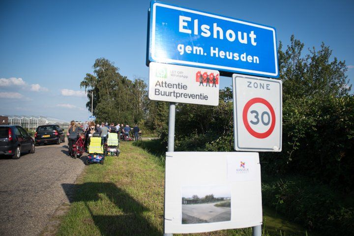 Verkeersbord voor Elshout, Nederland, met een snelheidslimiet van 30 km/u. Mensen met winkelwagens staan ​​langs de kant van de weg.