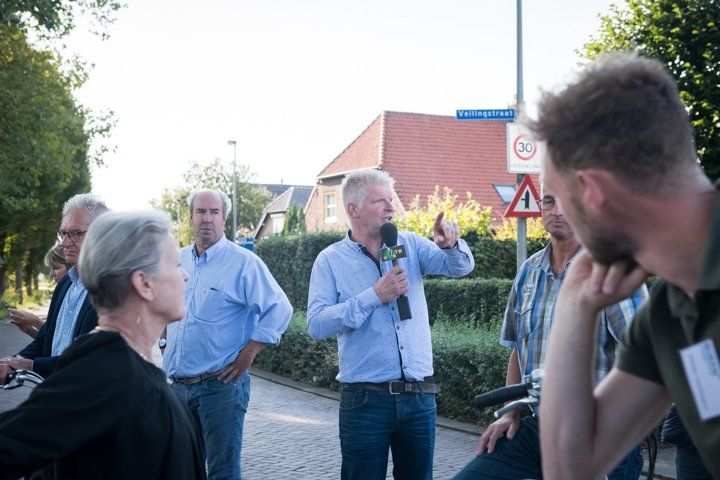 Een man met een microfoon spreekt een groep mensen op straat toe. Andere mensen staan ​​te luisteren.