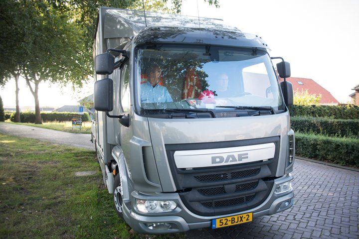 Grijze DAF-vrachtwagen geparkeerd op het gras, mensen in de cabine. Overdag, woonstraat.
