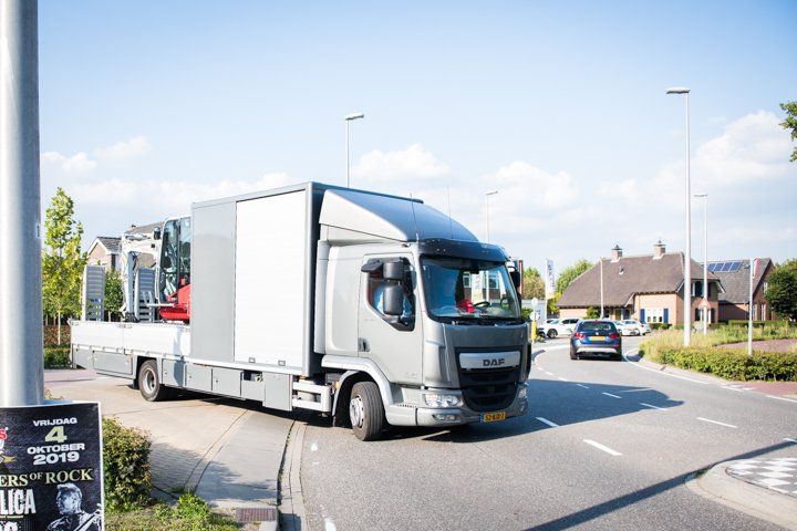Een DAF-vrachtwagen staat geparkeerd in een bocht, vlakbij een stoep met een reclamebord, in een woonwijk, op een zonnige dag.