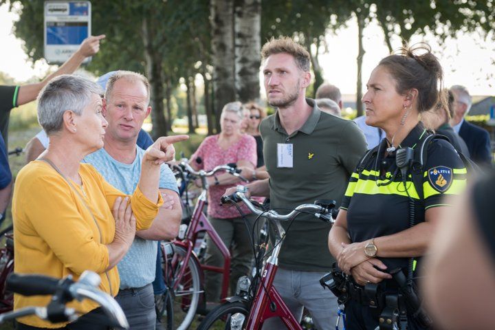Een groep mensen praat buiten met een politieagent, vlakbij geparkeerde fietsen.