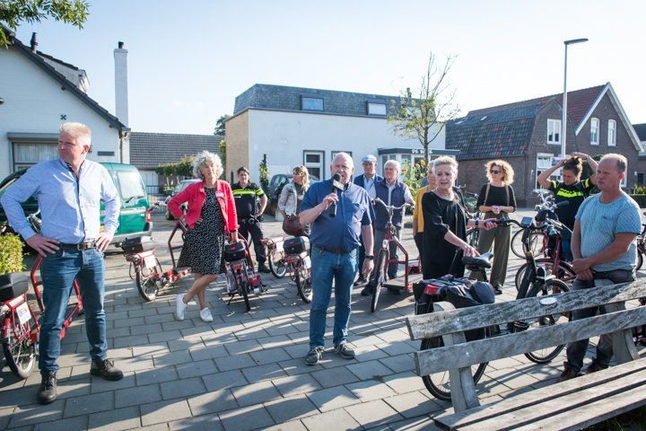 Een groep mensen op fietsen luistert buiten naar een man met een microfoon.
