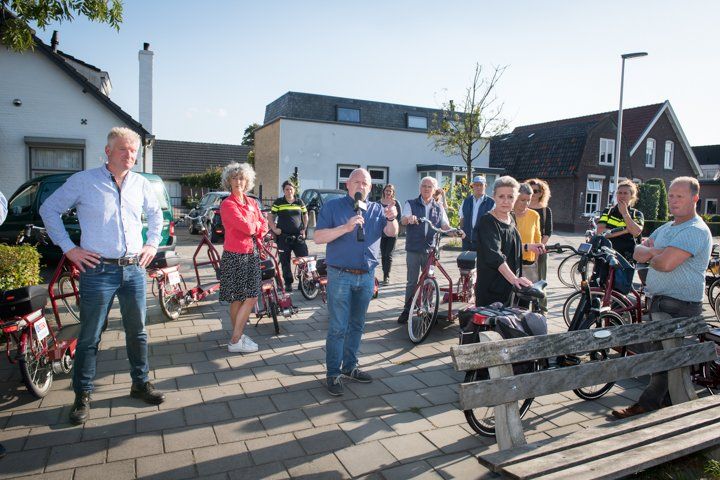 Een groep mensen op fietsen, waarvan er één in een microfoon spreekt. Buiten, zonnige dag.