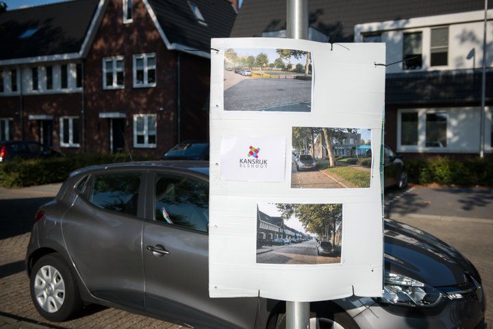 Een grijze auto met een bord waarop foto's van een pand voor een gebouw te zien zijn.