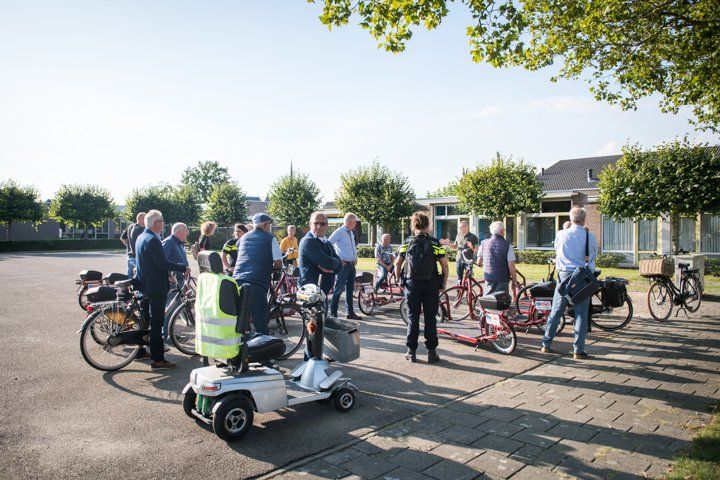 Een groep mensen met fietsen en scootmobielen verzamelde zich buiten op een zonnige dag.
